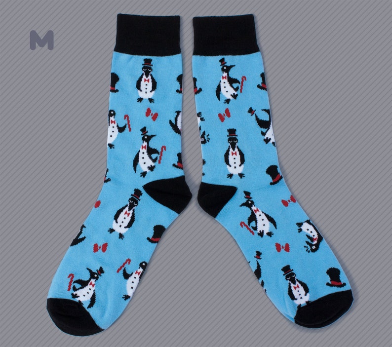 May include: A pair of blue socks with a pattern of penguins wearing top hats and bow ties. The socks have black cuffs.