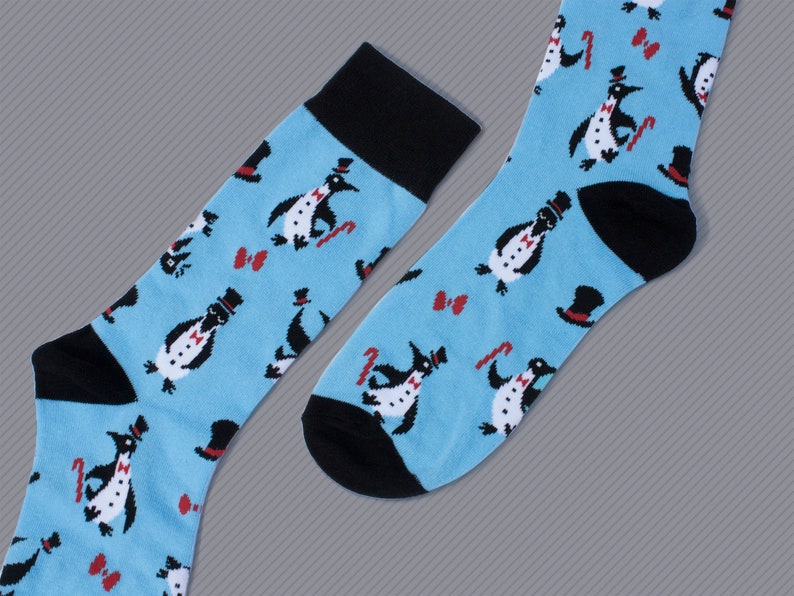 May include: A pair of blue socks with a penguin pattern. The penguins are wearing top hats and bow ties. The socks have black cuffs.