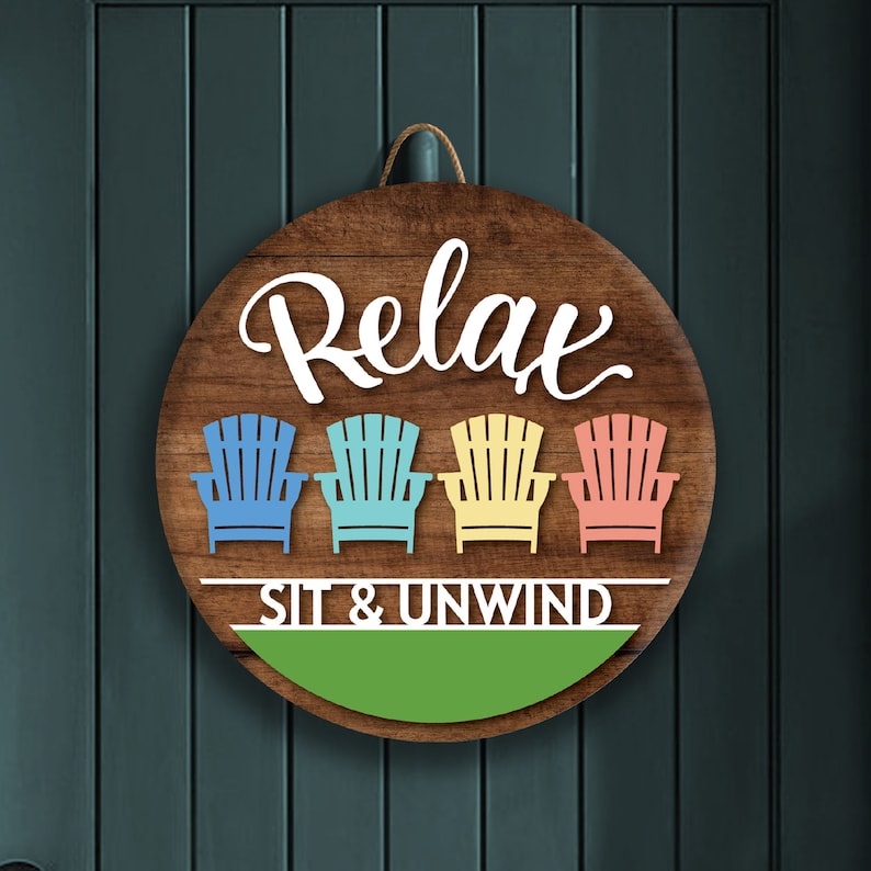 May include: A round wooden sign with the text "Relax Sit & Unwind" in white lettering. Four colorful beach chairs are depicted in a row above the text.