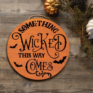 May include: A round wooden sign with the text "Something Wicked This Way Comes" in black lettering. The sign is decorated with bats and swirls.