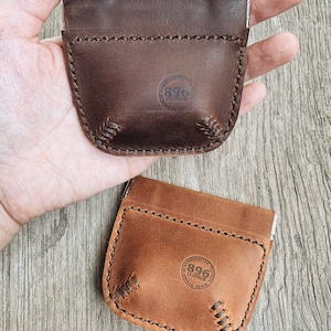 May include: Two leather coin purses with a snap closure. The purses are brown and tan and have a stitched baseball design. The purses have a circular logo that says "896 Leather".