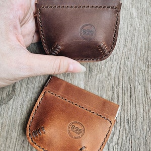 May include: Two leather coin purses with a stitched design. The purses are brown and tan and have a circular logo that says "896 Leather" on them.