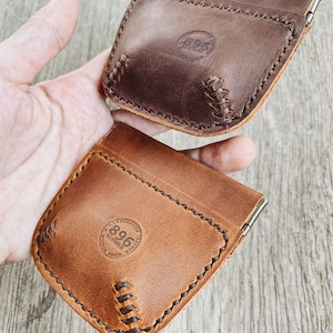 May include: Two brown leather wallets with a snap closure. The wallets have a stitched design and a circular logo with the text "896 Leather" on the front.