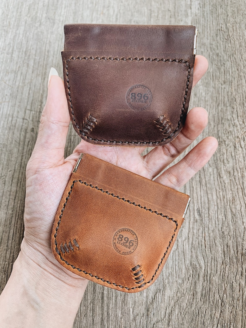 May include: Two leather coin purses with a snap closure. The purses are brown and tan and have a stitched design. The purses have a circular logo with the text "896 Leather" on them.