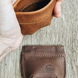 May include: Two leather coin purses, one brown and one dark brown, with a stitched edge and a small circular logo that says "Handmade 1996" in the center.