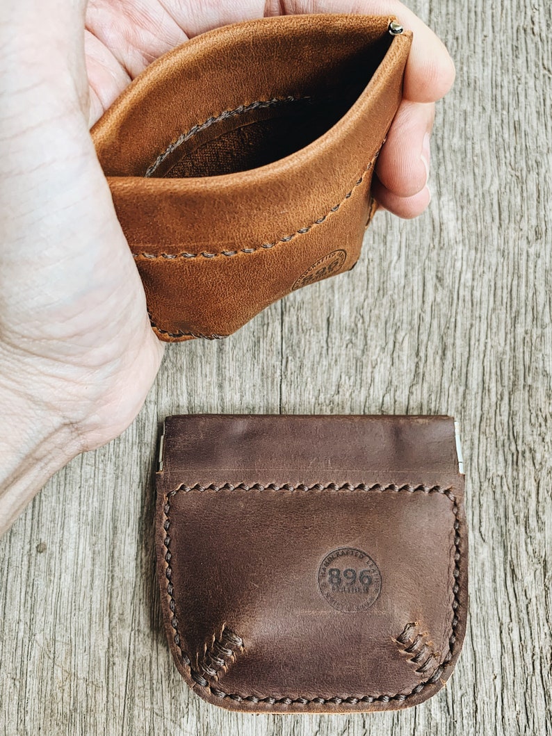 May include: Two leather coin purses, one brown and one dark brown, with a stitched edge and a small circular logo that says "Handmade 1996" in the center.