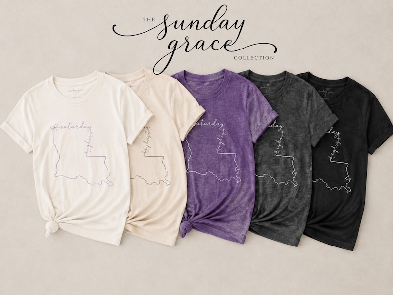 May include: Five short-sleeve t-shirts in cream, light beige, purple, dark gray, and black. Each shirt features a white line-art outline of the state of Louisiana with the word Saturday written horizontally and Sunday written vertically.