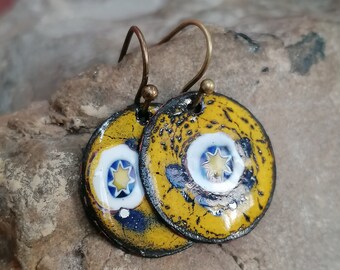 Può includere: Un paio di orecchini in smalto giallo con un design a stella bianca e blu. Gli orecchini hanno un aspetto invecchiato e sono attaccati a ganci dorati.