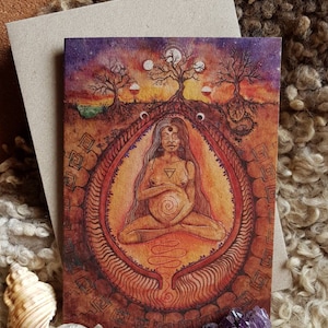 Könnte beinhalten: Eine Grußkarte mit einer Aquarellillustration einer schwangeren Person in meditativer Pose, umgeben von einem verzierten Design. Das Kunstwerk zeigt Bäume, Monde und eine warme Farbpalette aus Orange, Rot und Lila. Die Karte wird von einem schlichten Umschlag begleitet.