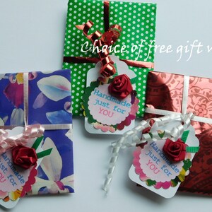 May include: Three small gift boxes wrapped in different patterned paper with matching ribbon and tags. The tags are decorated with a red flower and the text "Handmade just for YOU".