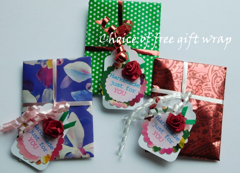 May include: Three small gift boxes wrapped in different patterned paper with matching ribbon and tags. The tags are decorated with a red flower and the text "Handmade just for YOU".