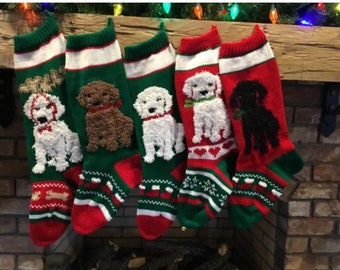 Puede incluir: Cuatro calcetines de Navidad con diferentes razas de perros bordadas. Los calcetines son rojos, verdes y blancos con un ribete blanco. Los perros son un caniche blanco, un caniche marrón, un caniche blanco y un labrador negro.
