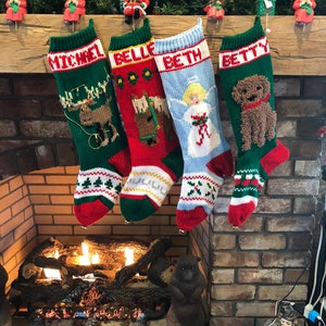Peut inclure: Quatre chaussettes de Noël en tricot avec les noms "Michel", "Belle", "Beth" et "Betty" accrochées à une cheminée en briques. Chaque chaussette présente un motif brodé différent, notamment un élan, un cheval, un ange et un chien.