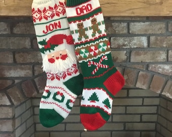 May include: Two knitted Christmas stockings hanging on a brick fireplace mantel. The stocking on the left is white with red and green accents and says "JON" on it. The stocking on the right is green with white and red accents and says "DAD" on it.