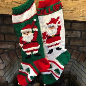 May include: Two red and green knitted Christmas stockings with Santa Claus designs. One stocking has the name "Callum" knitted into the cuff.