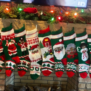 May include: Eight knitted Christmas stockings hanging on a fireplace mantel. The stockings are green, red, and white with various holiday designs, including Santa Claus, a snowman, a nutcracker, and a mailbox.