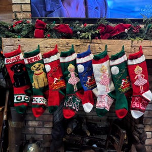 May include: Seven red, green, and white Christmas stockings with personalized names, "Rosie", "Beau", and others, hanging on a wooden mantel above a fireplace.