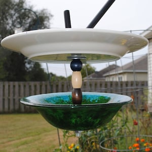 May include: A DIY bird feeder made from a white ceramic plate, a green glass bowl, and wooden dowels with black and white beads. The feeder is suspended from a black metal hook.