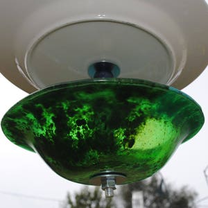 May include: A green glass bird feeder with a white ceramic top. The feeder has a mottled green finish and a metal hook for hanging.