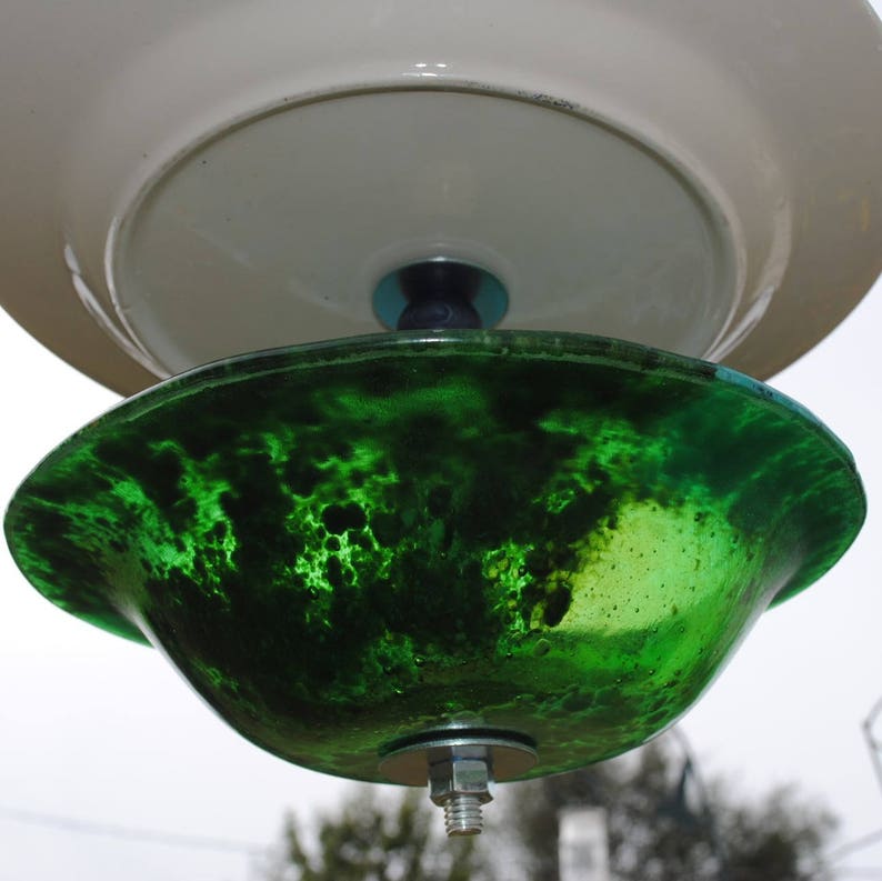 May include: A green glass bird feeder with a white ceramic top. The feeder has a mottled green finish and a metal hook for hanging.