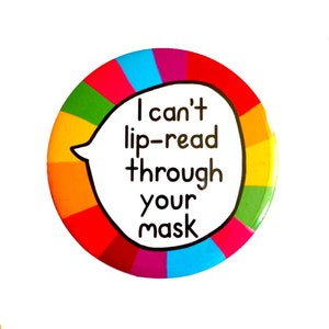 Puede incluir: Un botón redondo con un borde de arcoíris y una burbuja de diálogo blanca en el centro. La burbuja de diálogo dice "No puedo leer los labios a través de tu máscara."