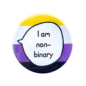 Puede incluir: Un botón redondo con los colores de la bandera del orgullo no binario: amarillo, blanco, morado y negro. El botón tiene un globo de diálogo blanco con el texto "Soy no binario" en negro.