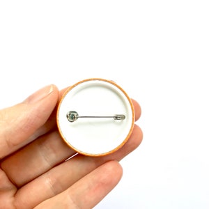May include: The back of a round orange button with a white centre and a silver safety pin.