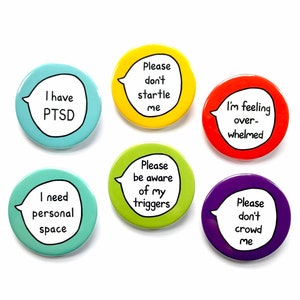 Puede incluir: Seis botones redondos con diferentes mensajes sobre la salud mental. Los botones son de varios colores, incluyendo azul, verde, amarillo, rojo y morado. Los mensajes en los botones incluyen "Tengo PTSD", "Necesito espacio personal", "Por favor, no me asustes", "Por favor, sé consciente de mis detonantes", "Me siento abrumado", y "Por favor, no me agobies".