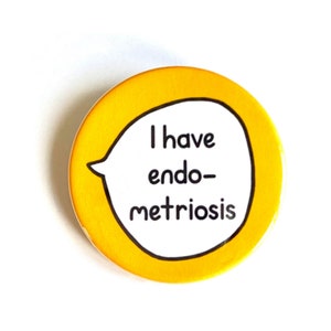 May include: A circular, yellow badge with a white speech bubble. The text "I have endometriosis" is written in black. The badge has a black outline and a pin fastening.