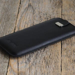 May include: Black leather phone case with a zipper closure and a silver metal pull tab. The case has the word "Alcantara" embossed on the front.