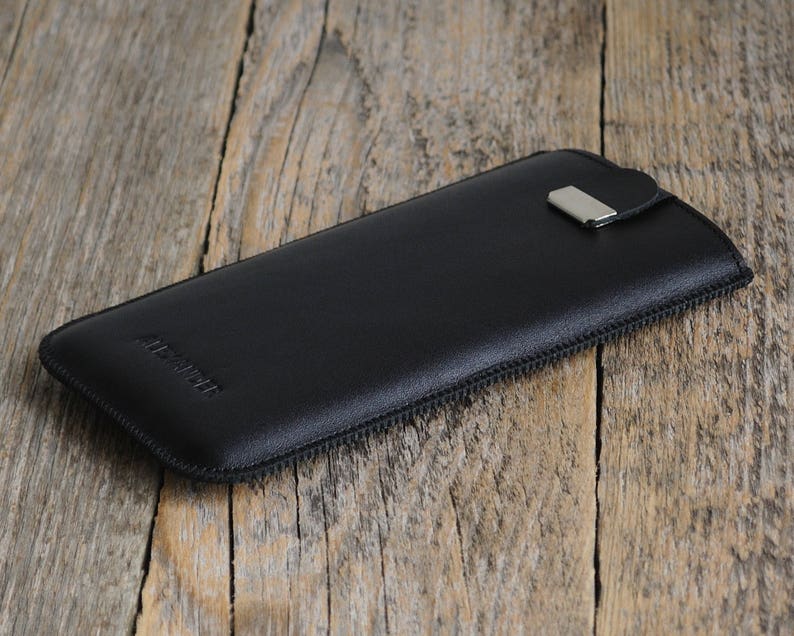May include: Black leather phone case with a zipper closure and a silver metal pull tab. The case has the word "Alcantara" embossed on the front.