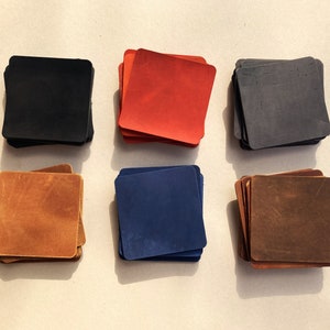 Peut inclure: Six piles de sous-verres en cuir de différentes couleurs. Les sous-verres sont carrés et ont une finition lisse et polie. Les couleurs sont le noir, le rouge, le bleu, le marron et le beige.