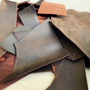 May include: A pile of brown leather scraps in various sizes and shapes. The leather is a mix of dark brown, light brown, and reddish brown.