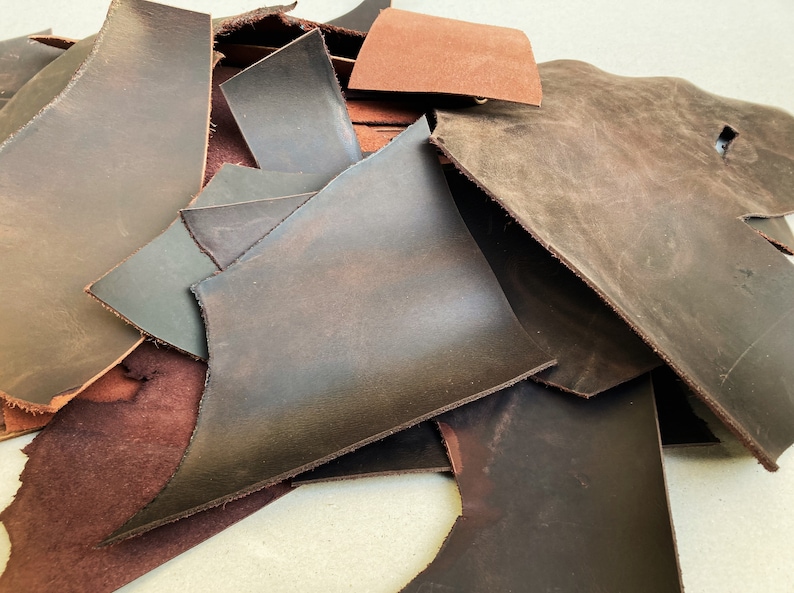 May include: A pile of brown leather scraps in various sizes and shapes. The leather is a mix of dark brown, light brown, and reddish brown.