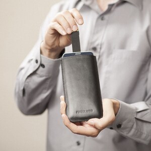 May include: A black leather phone case with a flap closure. The case has the text "Finger Welt" embossed on the front.