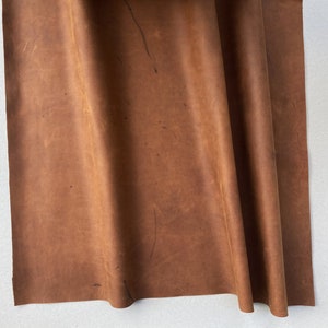 May include: A piece of brown leather folded in thirds. The leather has a natural, rustic look with some visible marks and scratches.