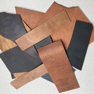 May include: Assortment of leather scraps in various shades of brown and black. The leather pieces are arranged in a pile on a white surface.