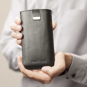 Könnte beinhalten: Eine schwarze Leder Handyhülle mit einem silbernen Verschluss und dem Text "Finger Weg" geprägt auf der Vorderseite.