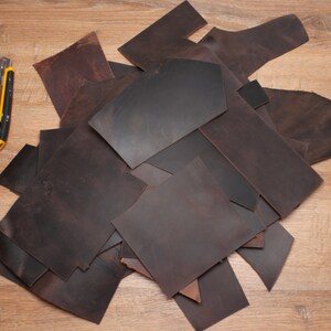 May include: A pile of brown leather scraps on a wooden surface. A yellow utility knife is visible in the background.
