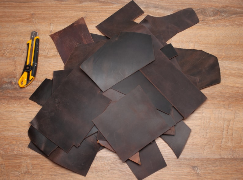 May include: A pile of brown leather scraps on a wooden surface. A yellow utility knife is visible in the background.