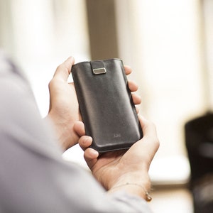 May include: A black leather phone case with a silver clasp. The case is being held in someone's hands.