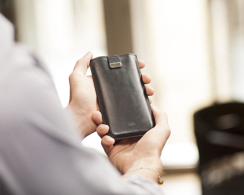 May include: A black leather phone case with a silver clasp. The case is being held in someone's hands.