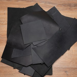 May include: A pile of black leather scraps on a wooden surface. A yellow utility knife is also visible in the image.
