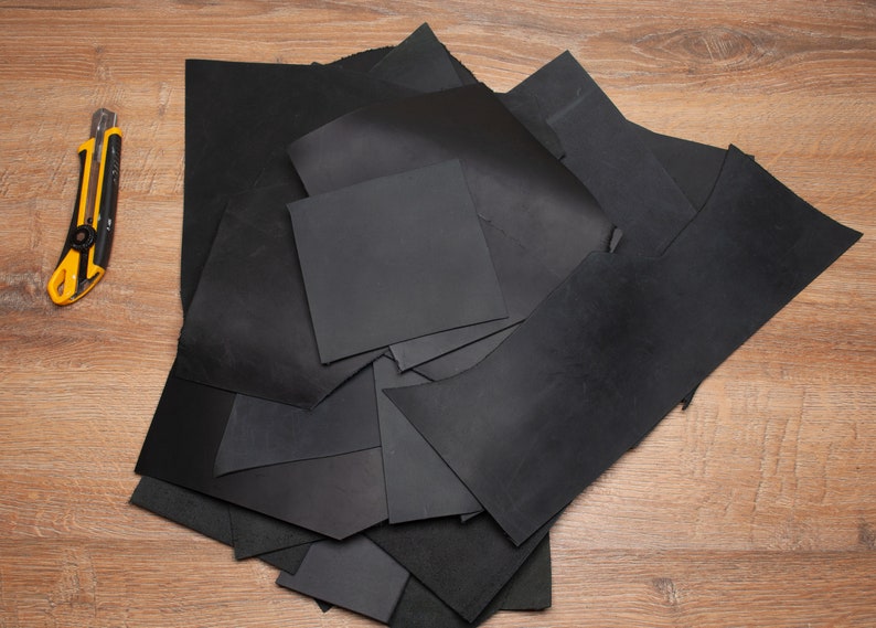 May include: A pile of black leather scraps on a wooden surface. A yellow utility knife is also visible in the image.