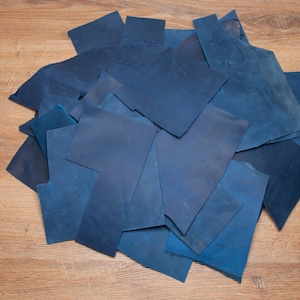 May include: A pile of blue fabric scraps on a wooden surface. The fabric is a deep blue color and has a slightly textured surface.