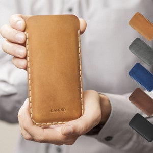Può includere: Una custodia per telefono in pelle marrone con cuciture bianche e la parola "CAMINO" impressa sul retro.