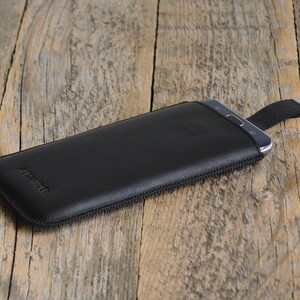 May include: Black leather phone case with a zipper and a strap. The case has the word "ARCTIC" embossed on the front.