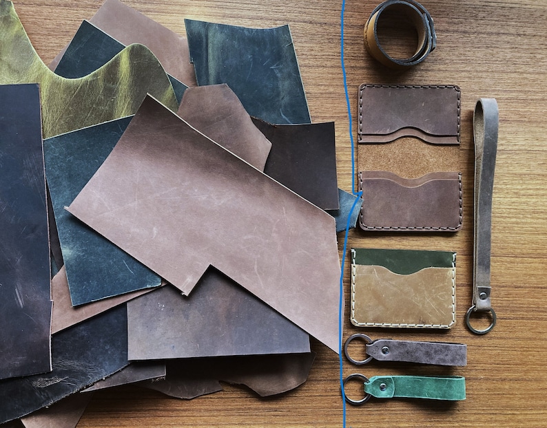 May include: Assortment of leather pieces in various shades of brown, green, and black, including scraps and finished pieces.  There are also three leather card holders and a leather key chain with a key ring.