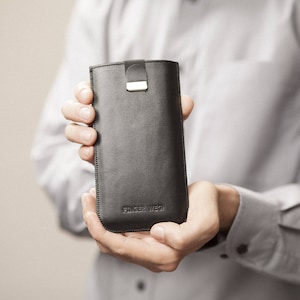 May include: A black leather phone case with a gold clasp and the text "FINGER WEG" embossed on the bottom.