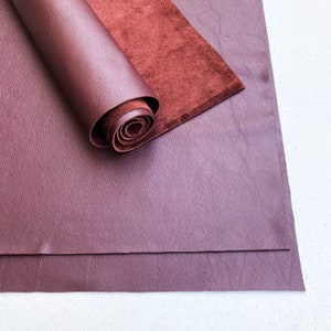 Puede incluir: Dos piezas de tela de cuero burdeos, una enrollada y la otra plana.